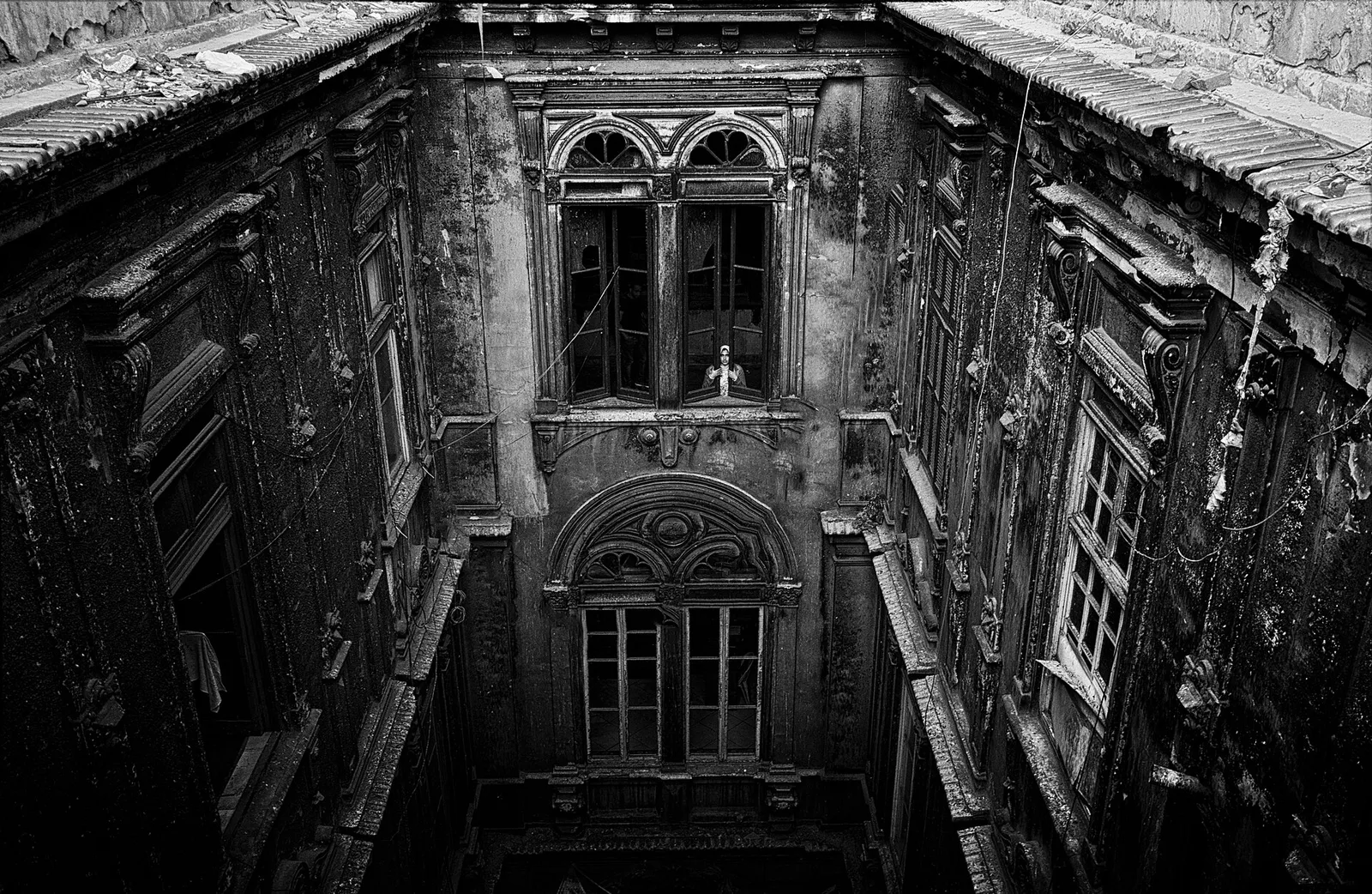 فناء داخلي لعمارة سكندرية عريقة متهالكة، وساكنة تطل من إحدى نوافذها