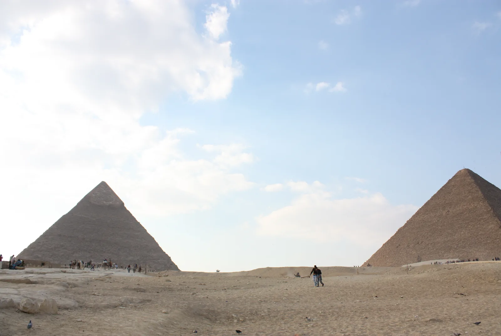 هرما خوفو وخفرع يرتفعان فوق هضبة الجيزة كما يبدوان من مستوى الأرض، وزائر يسير على الرمال بينهما