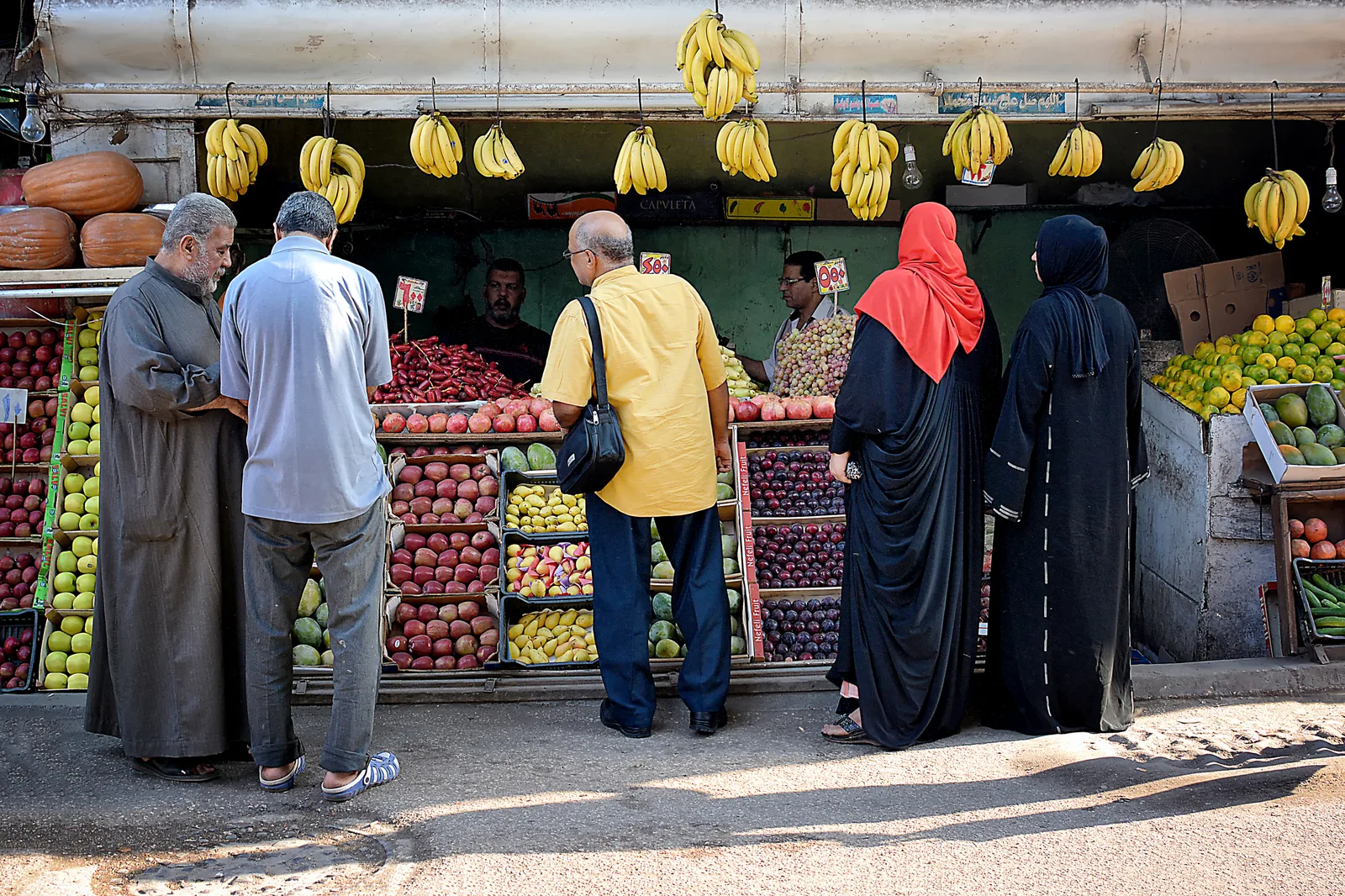 متسوقون مصريون أمام محل فاكهة معلّق عليه عناقيد الموز، وصناديق التفاح والرمان مرصوصة أمامه